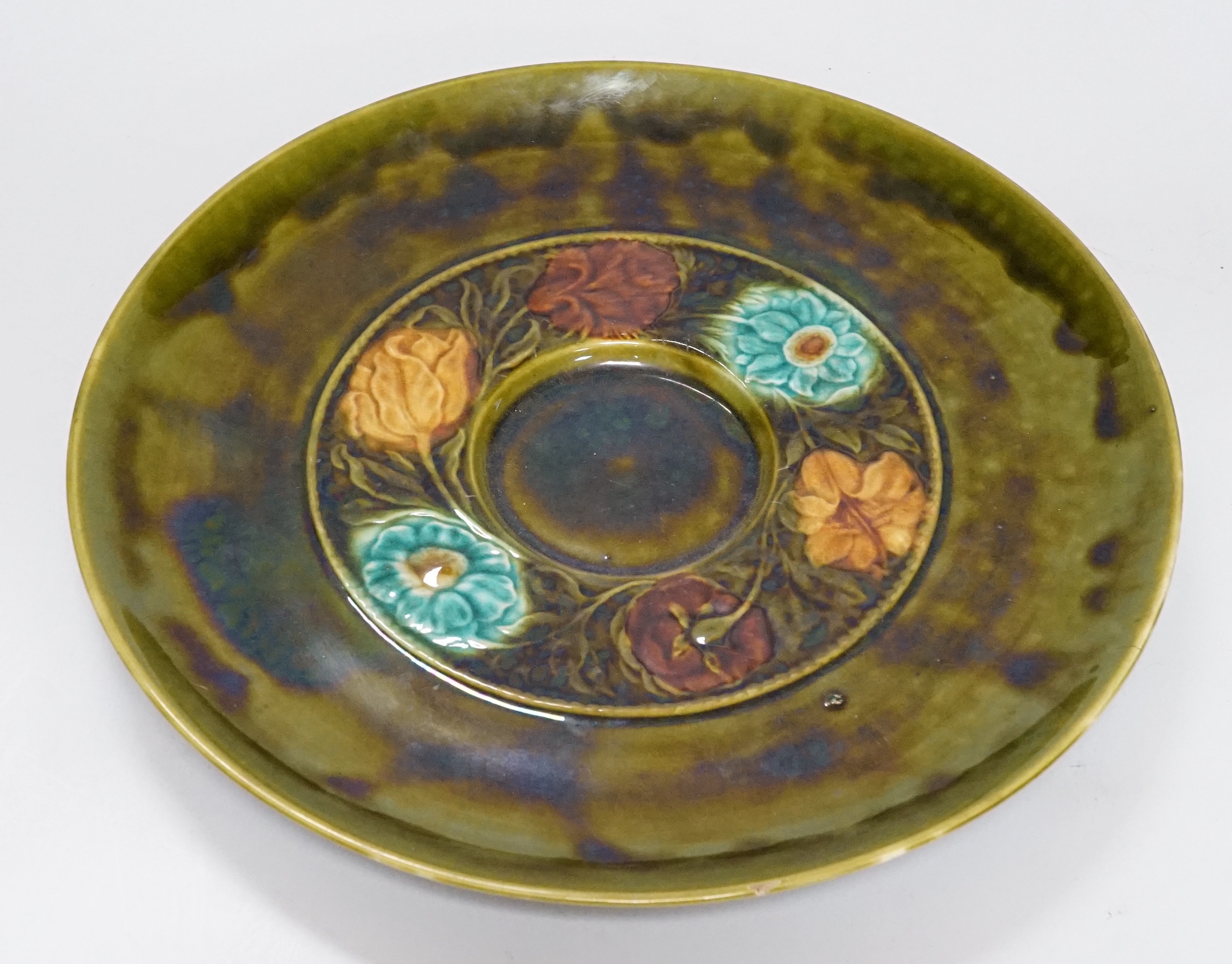 Christopher Dresser for Linthorpe, an art pottery, Aesthetic Movement plate, majolica glazed relief design with a central wreath of flowers, highlighted in turquoise, brown and yellow against a green ground, signature an